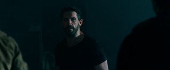 Movie still from “Triple Threat” (2019), directed by Jesse V. Johnson – A man in a black shirt is standing in a dark room; Medium shot, Over the shoulder angle