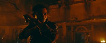 Movie still from “Triple Threat” (2019), directed by Jesse V. Johnson – A man standing in the dark with his hand to his face; Close Up shot, Over the shoulder angle