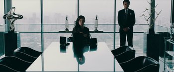 Movie still from “Triple Threat” (2019), directed by Jesse V. Johnson – A woman sitting at a table in front of a large window; Medium shot, Over the shoulder angle