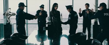 Movie still from “Triple Threat” (2019), directed by Jesse V. Johnson – A group of men standing around a woman in a room; Medium shot, Over the shoulder angle