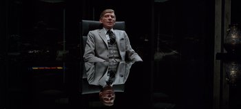 Movie still from “Tron” (1982), directed by Steven Lisberger – A man in a suit sitting on a chair in front of a mirror; Medium shot, Low angle