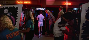 Movie still from “Tron” (1982), directed by Steven Lisberger – A group of people standing in front of a tv; Wide shot, Over the shoulder angle