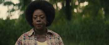 An older woman with a large afro is standing in a park