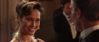 Movie still from “True Lies” (1994), directed by James Cameron – A beautiful woman smiling at the camera while a man in a suit stands in the background; Close Up shot, Over the shoulder angle