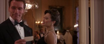 Movie still from “True Lies” (1994), directed by James Cameron – A woman in a black dress with a necklace and earrings; Medium shot, Over the shoulder angle