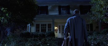 Movie still from “True Lies” (1994), directed by James Cameron – A man in a blue coat standing in front of a house at night; Wide shot, Low angle