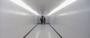 Movie still from “True Lies” (1994), directed by James Cameron – Two men in suits walk down a long hallway; Extreme Wide shot, High angle