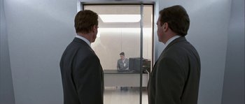 Movie still from “True Lies” (1994), directed by James Cameron – Two men in suits are looking at a man in a suit; Wide shot, Low angle