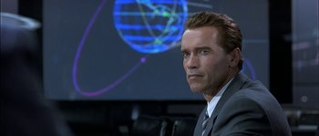 Movie still from “True Lies” (1994), directed by James Cameron – A man in a business suit sitting in front of a projection screen; Close Up shot, Low angle