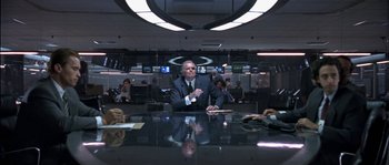 Movie still from “True Lies” (1994), directed by James Cameron – A man sitting at a table in front of other people; Wide shot, Low angle