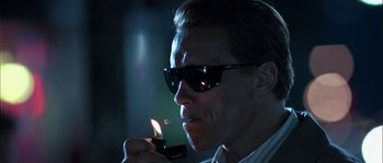 Movie still from “True Lies” (1994), directed by James Cameron – A man in sunglasses is lighting a cigarette; Close Up shot, Low angle