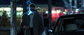 Movie still from “True Lies” (1994), directed by James Cameron – A man smoking a cigarette while standing in front of a car; Medium shot, Low angle