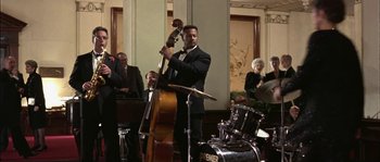 Movie still from “True Lies” (1994), directed by James Cameron – A man in a suit playing a double bass; Medium shot, Low angle