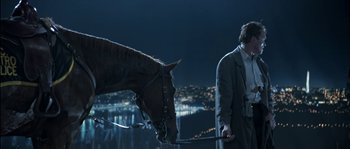 Movie still from “True Lies” (1994), directed by James Cameron – A man standing next to a horse on a field; Wide shot, Over the shoulder angle