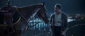 Movie still from “True Lies” (1994), directed by James Cameron – A man standing next to a horse on a city street at night; Medium shot, Over the shoulder angle