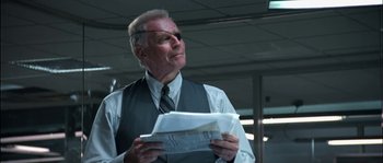Movie still from “True Lies” (1994), directed by James Cameron – An older man in a vest and tie reading a newspaper; Close Up shot, Low angle
