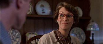 Movie still from “True Lies” (1994), directed by James Cameron – A woman wearing glasses sitting in a chair; Close Up shot, Low angle