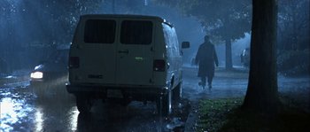Movie still from “True Lies” (1994), directed by James Cameron – A man walking down a street next to a white van; Wide shot, Low angle