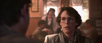 Movie still from “True Lies” (1994), directed by James Cameron – A woman wearing glasses and a suit and tie; Close Up shot, Over the shoulder angle