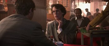 Movie still from “True Lies” (1994), directed by James Cameron – A person sitting at a table with a drink; Medium shot, Over the shoulder angle