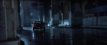 Movie still from “True Lies” (1994), directed by James Cameron – A car is parked on the side of the road in the rain; Wide shot, High angle