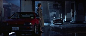 Movie still from “True Lies” (1994), directed by James Cameron – A woman standing next to a red car in a parking lot; Wide shot, Low angle