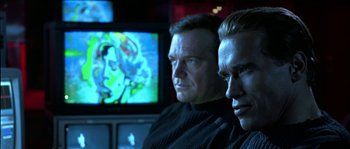 Movie still from “True Lies” (1994), directed by James Cameron – Two men sitting in front of a tv in a room; Close Up shot, Low angle