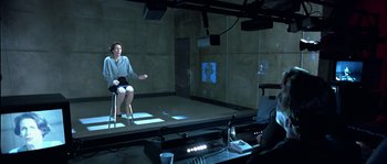 Movie still from “True Lies” (1994), directed by James Cameron – A woman sitting on a chair in front of a projection screen; Wide shot, Over the shoulder angle