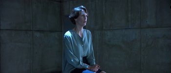 Movie still from “True Lies” (1994), directed by James Cameron – A woman sitting on a chair in a dark room; Medium shot, Low angle