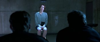 Movie still from “True Lies” (1994), directed by James Cameron – A woman sitting on a stool in a dark room; Medium shot, Over the shoulder angle
