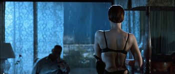 Movie still from “True Lies” (1994), directed by James Cameron – A woman standing in front of a man in a dark room; Medium shot, Over the shoulder angle