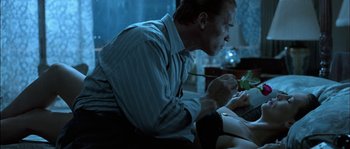 Movie still from “True Lies” (1994), directed by James Cameron – A man sitting at a table with a pen in his mouth; Medium shot, Over the shoulder angle