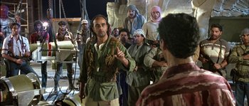 Movie still from “True Lies” (1994), directed by James Cameron – A group of people standing in a room; Medium shot, Over the shoulder angle