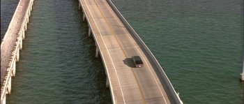 Movie still from “True Lies” (1994), directed by James Cameron – An aerial view of a car driving on a bridge over a body of water; Extreme Wide shot, High angle