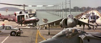 Movie still from “True Lies” (1994), directed by James Cameron – Two airplanes are parked on a runway next to a body of water; Wide shot, Low angle