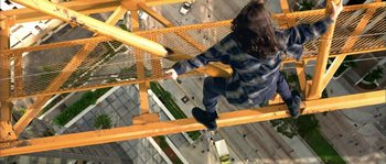 Movie still from “True Lies” (1994), directed by James Cameron – A man hanging from a metal structure on top of a building; Wide shot, Overhead angle