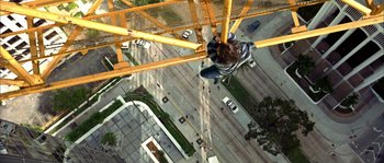 Movie still from “True Lies” (1994), directed by James Cameron – A man hanging from a crane over a city street; Wide shot, Overhead angle