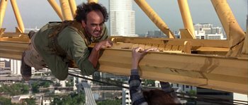 Movie still from “True Lies” (1994), directed by James Cameron – A man on a crane holding onto a metal beam; Medium shot, High angle