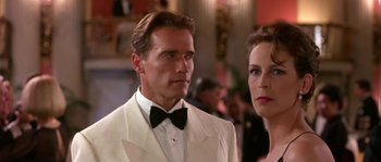 Movie still from “True Lies” (1994), directed by James Cameron – A man and a woman in a white suit and black bow tie; Close Up shot, Low angle