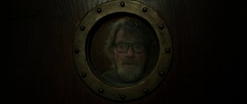 A man with a beard and glasses looking through a porthole