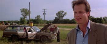 Movie still from “Twister” (1996), directed by Jan de Bont – A man standing in front of an old car; Medium shot, Over the shoulder angle