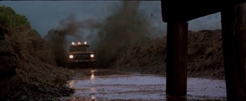 Movie still from “Twister” (1996), directed by Jan de Bont – A truck driving down a muddy road near a person in black pants; Extreme Wide shot, Low angle