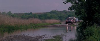 Movie still from “Twister” (1996), directed by Jan de Bont – A truck driving down a road next to a body of water; Extreme Wide shot, High angle