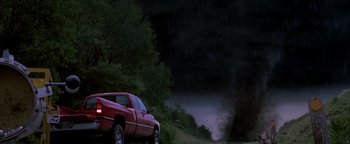 Movie still from “Twister” (1996), directed by Jan de Bont – A red pickup truck driving down a road near a forest; Extreme Wide shot, Low angle
