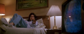Movie still from “Twister” (1996), directed by Jan de Bont – A woman sitting on a bed holding a remote control; Medium shot, High angle