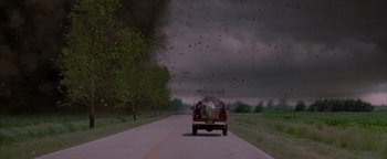 Movie still from “Twister” (1996), directed by Jan de Bont – A truck driving down a road near a forest; Extreme Wide shot, Low angle