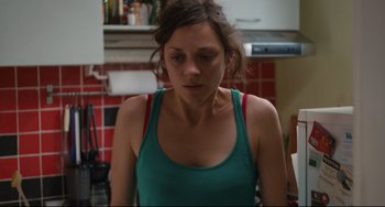 Movie still from “Two Days, One Night” (2014), directed by Jean-Pierre Dardenne – A woman in a green tank top is standing in a kitchen; Close Up shot, Over the shoulder angle