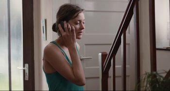 Movie still from “Two Days, One Night” (2014), directed by Jean-Pierre Dardenne – A woman is talking on a phone while standing next to stairs; Close Up shot, Over the shoulder angle