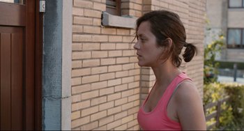 Movie still from “Two Days, One Night” (2014), directed by Jean-Pierre Dardenne – A woman in a pink tank top is standing by a brick wall; Close Up shot, Over the shoulder angle
