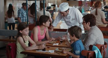 Movie still from “Two Days, One Night” (2014), directed by Jean-Pierre Dardenne – A man serving pizza to a group of people at a restaurant; Medium shot, Over the shoulder angle